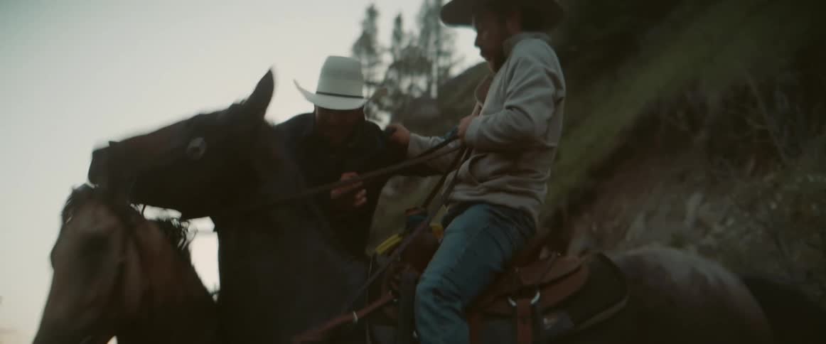 Two cowboys at dusk playing around on horses smiling and shoving each other in the woods