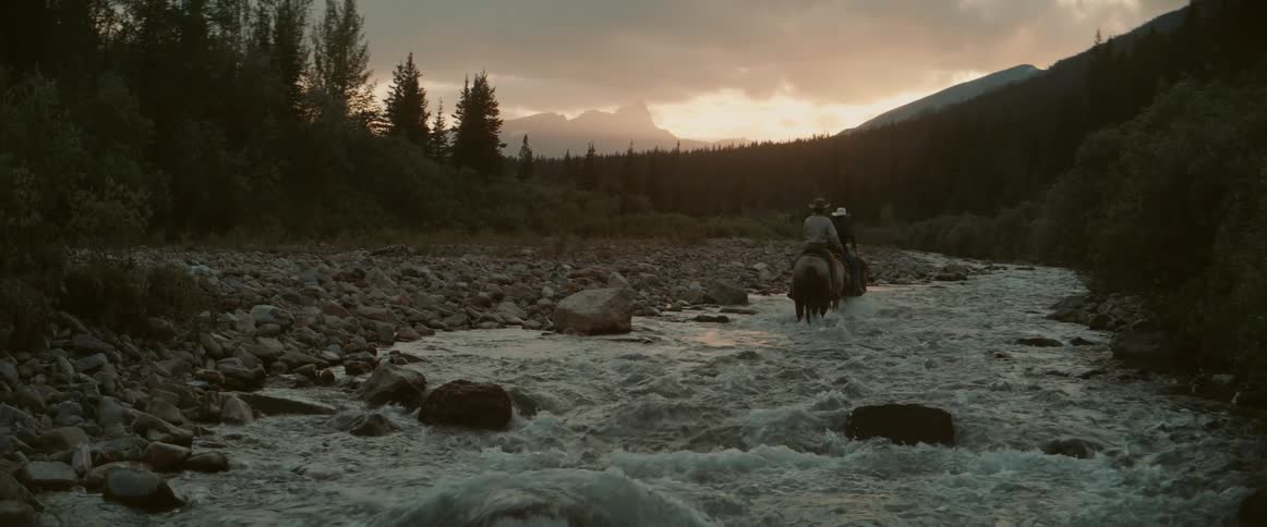 Two people riding horses and crossing a river
