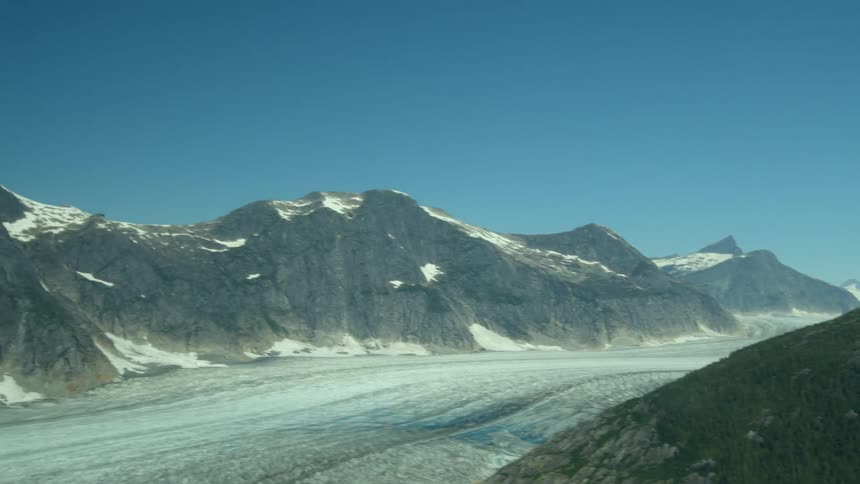 Snow capped mountains rise above a vast glacier under a clear blue sky