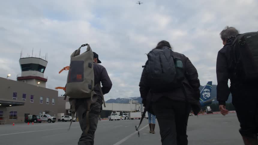 Three travelers with backpacks walking in an outdoor area of an airport