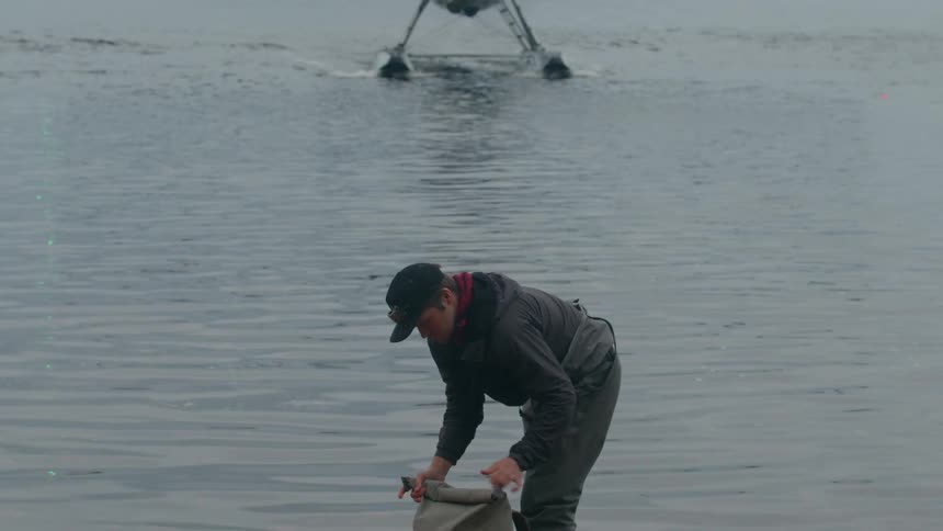 Man closing a backpack by a lake