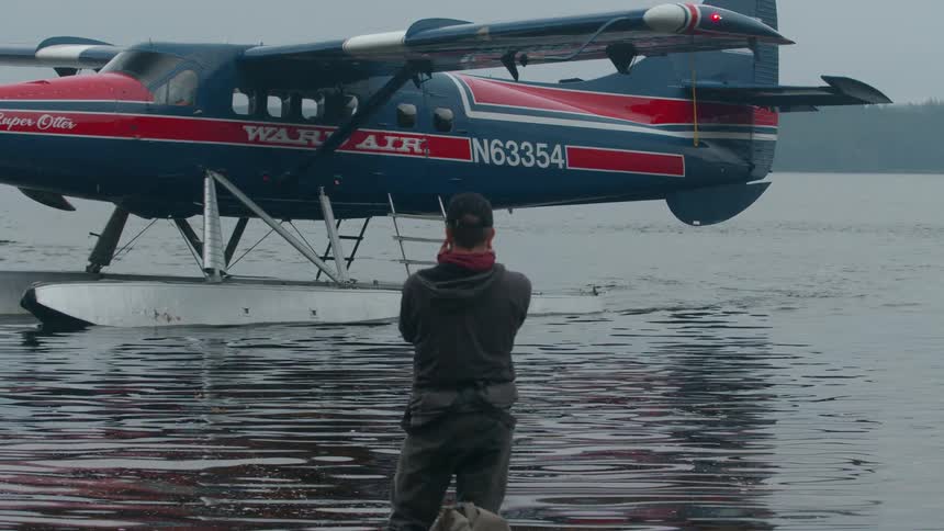 A de havilland canada dhc3 otter floatplane on the lake turns to take off with a person standing in front of it at midday