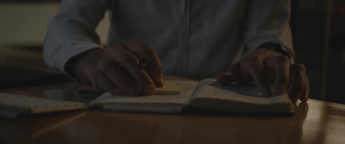 Man sitting at desk holding pen and looking at notebook