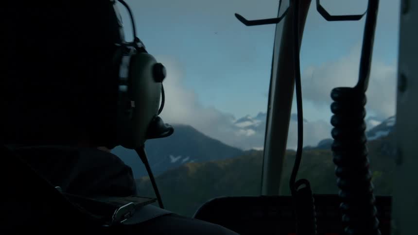 Person in the cockpit of a helicopter flying over mountains