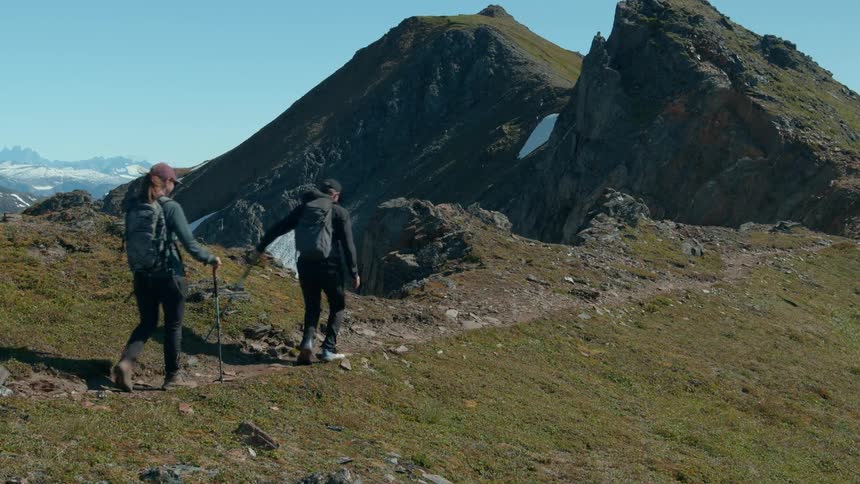 Two hikers walk along a rugged mountain trailand one hiker jumps in the air