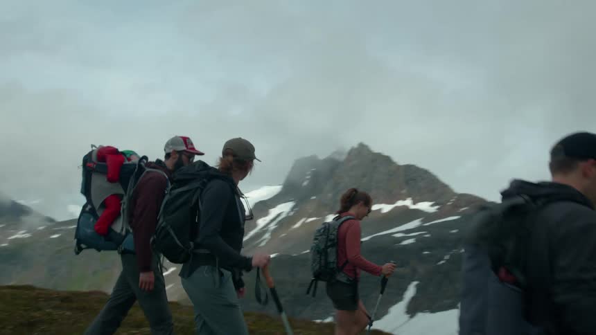 Group of hikers trek through a misty mountain trail toward snowy peaks