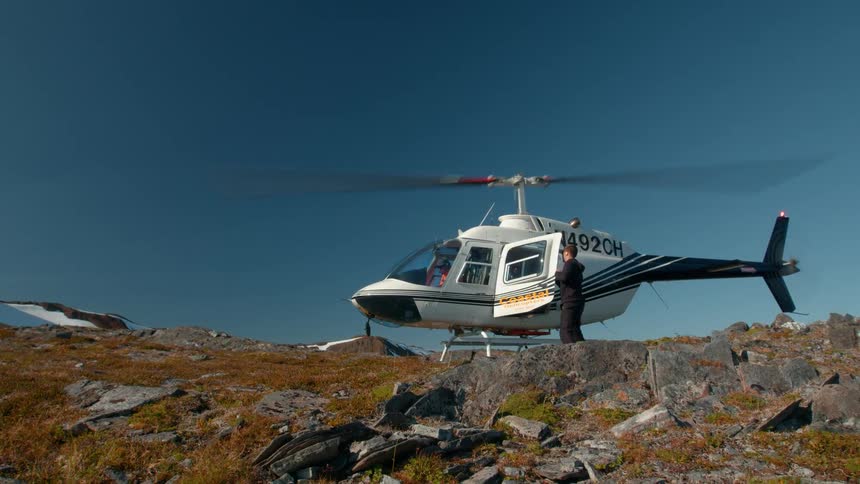 Two people descending from a helicopter in a mountain area