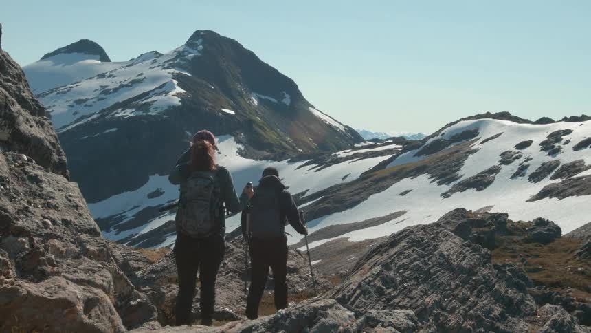 Two hikers explore a rocky snowcovered mountain trail under a clear sky