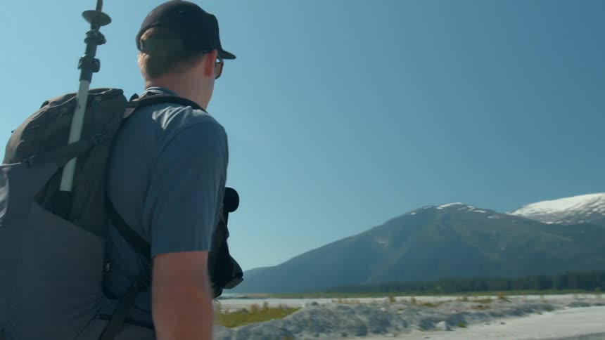 Man with backpack and tripod looks at snow capped mountains