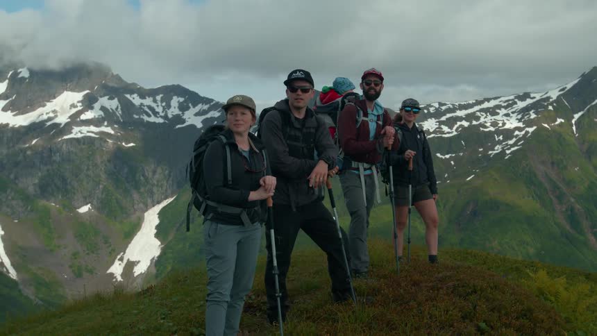 Hikers posing on grassy ridge with snowy mountains behind