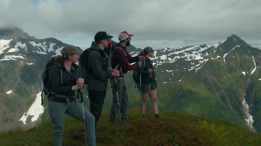 A group of hikers pause on a mountain peak admiring the scenic snow covered range