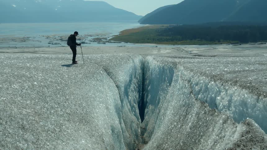Lone hiker walks on glacier near deep crevasse