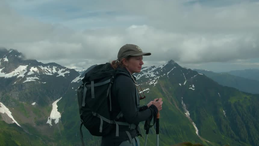 A hiker stands on a mountain ridge taking in the surrounding alpine landscape