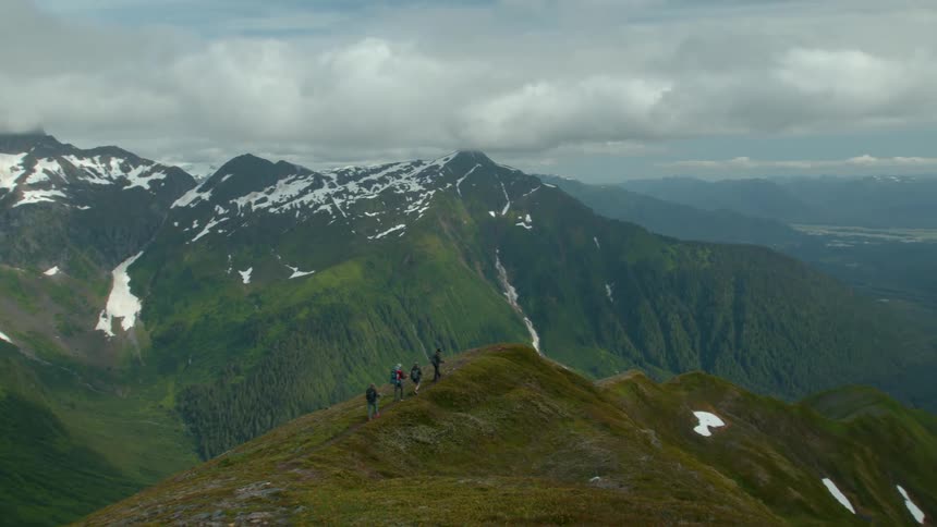 Hikers walk along a mountain ridge with snowy peaks in the background