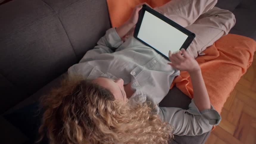 A woman relaxes on a couch while browsing a tablet