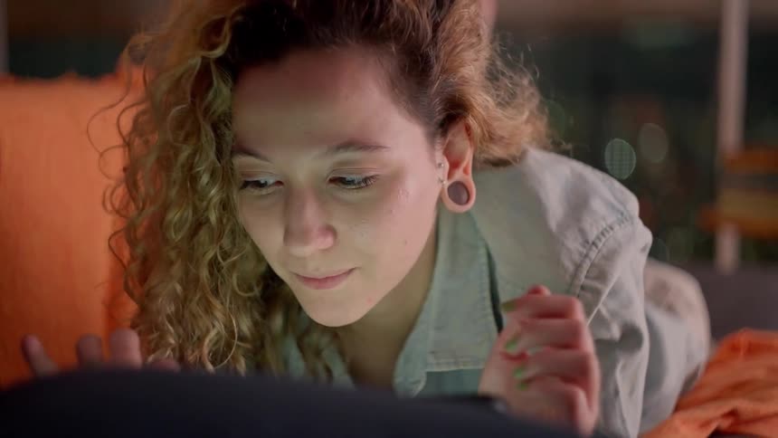 A female resting on a couch looks at a laptop