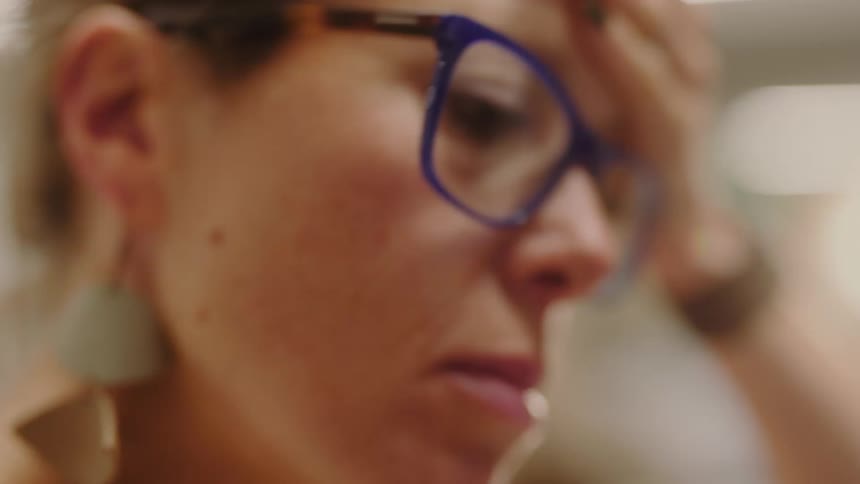 Woman wearing blue glasses and large gray earrings is seen in closeup