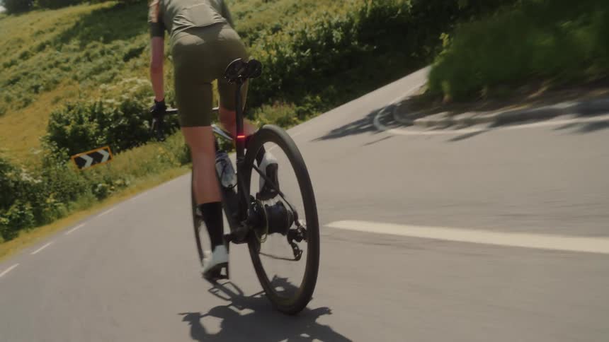 A woman in green clothes and cycles hard out of the saddle up a hill