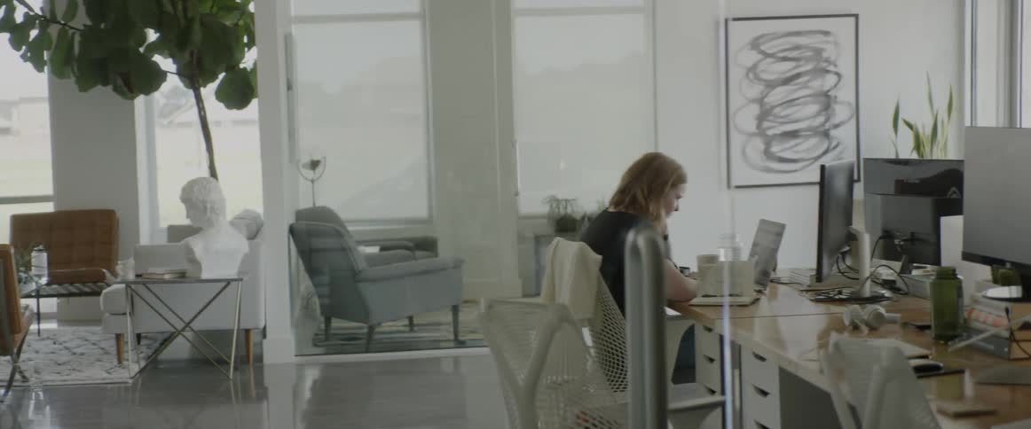 A woman sits at a desk and works on a laptop