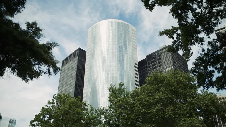 Glass skyscraper surrounded by trees under a partly cloudy sky