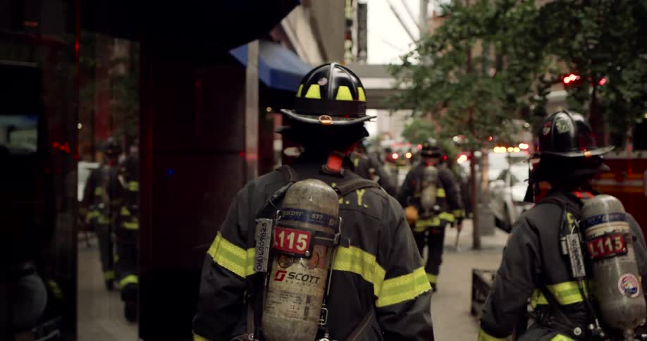 Firefighters in full gear walk down a city street toward a red fire truck
