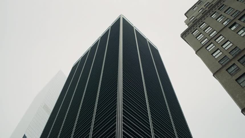 Modern skyscraper with glass facade and vertical lines is seen from below on a cloudy day