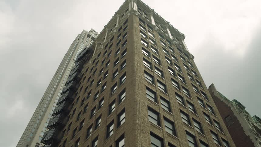 Skyscrapers rise behind leafy trees under a cloudy sky