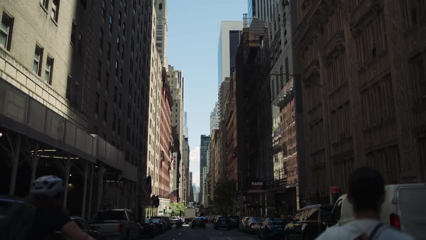 A busy city street is lined with tall buildings and scattered traffic