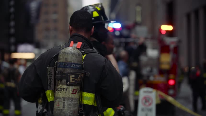 Firefighters stand on a city street near fire trucks during an emergency response