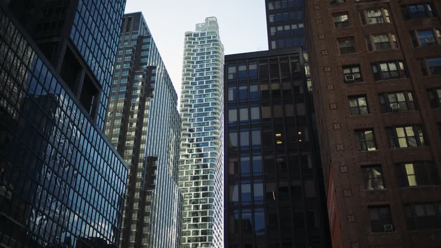 A slender modern skyscraper with a wavy textured white facade stands tall among other dark glass buildings in a city