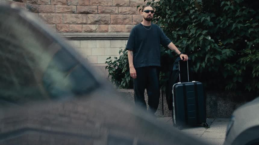 Man wearing black clothing and sunglasses holding a suitcase