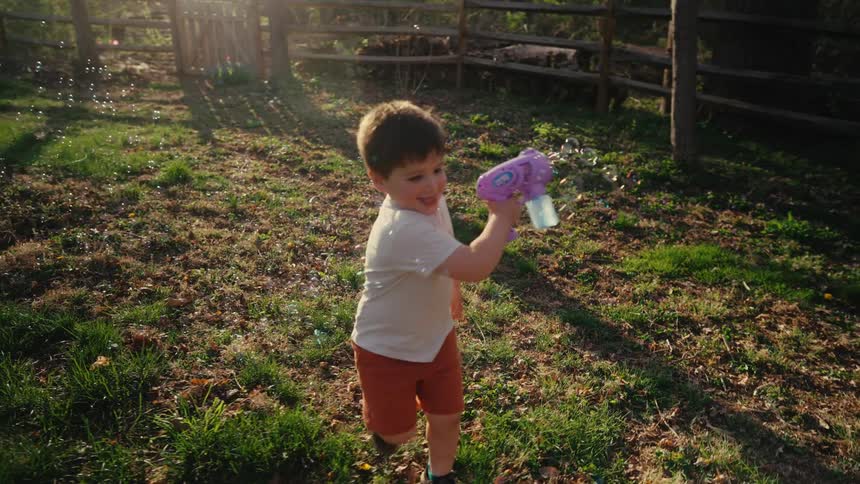 A young boy smiles while running with a bubble wand in a sunny yard