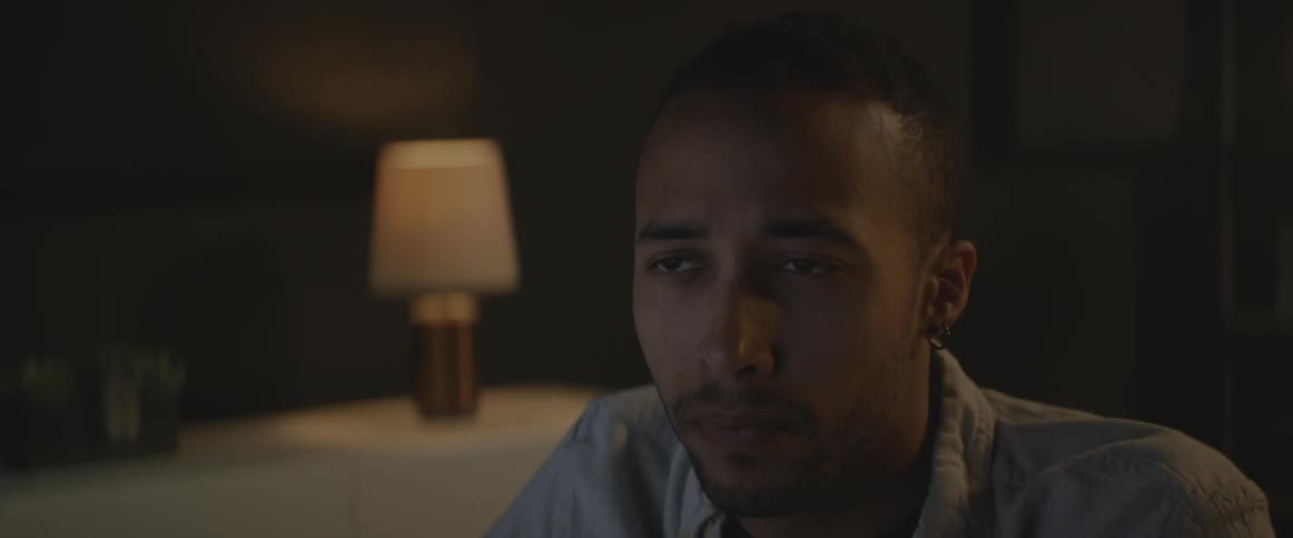A man in a darkened room appears to be listening and thinking