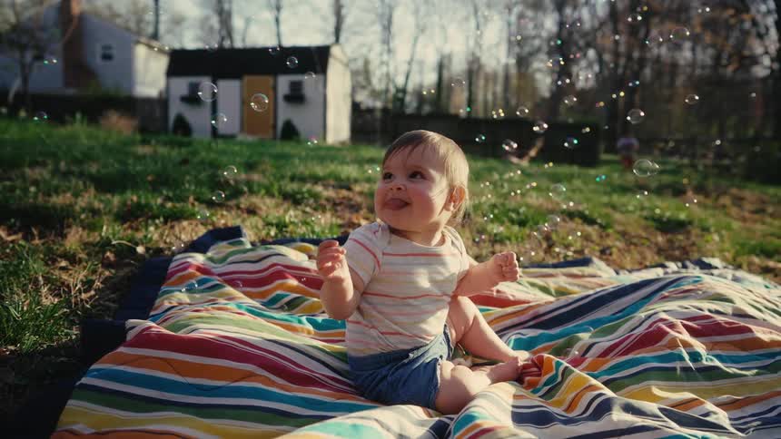 Little baby girl sitting outdoors with soap bubbles flying