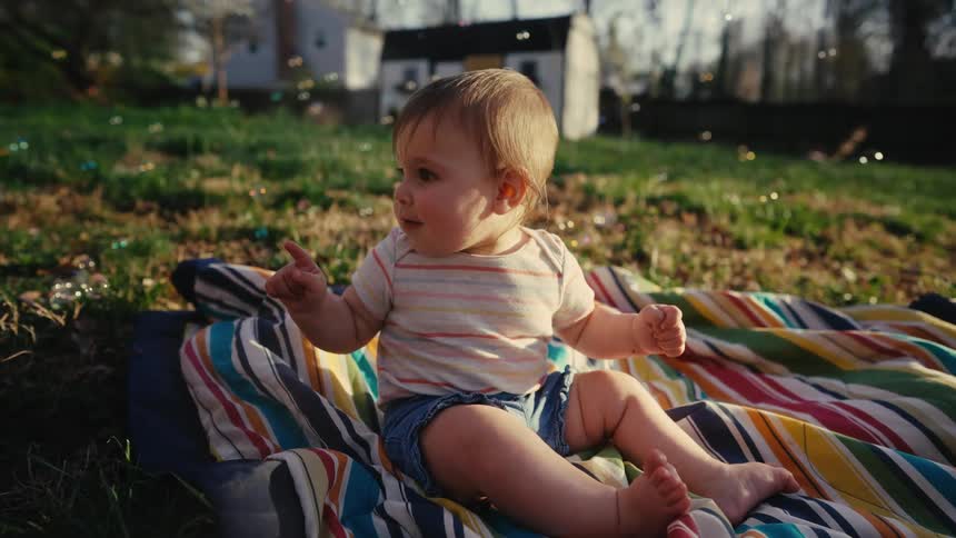 Baby girl sitting on a blanket on the lawn enjoying bubbles floating by