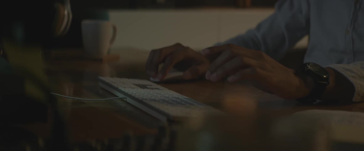 Man sitting at desk using computer mouse and typing on keyboard