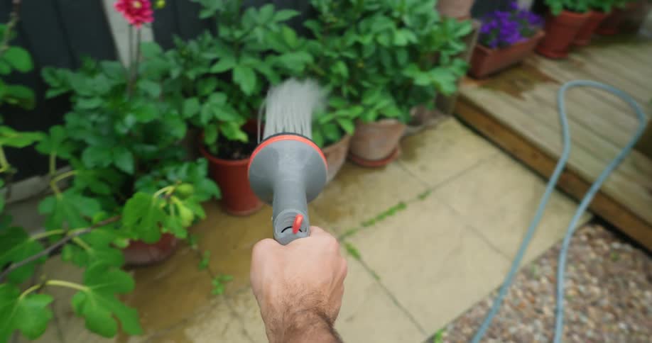 A man waters potted plants with a sprinkler device in a garden outdoors during daytime