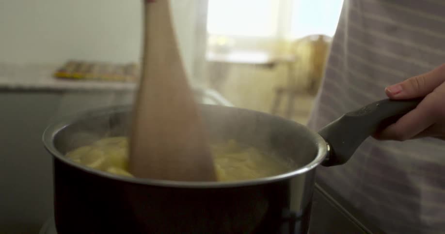 A woman stirs pasta cooking on a stovetop