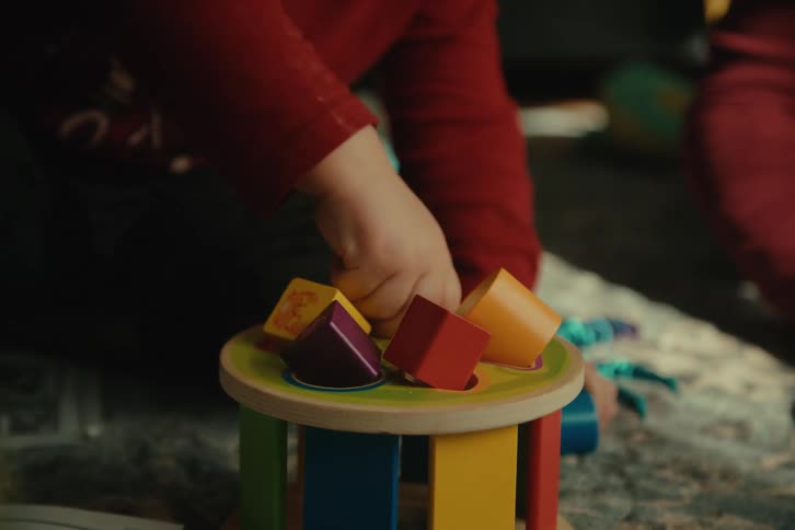 Pair of hands of a child sitting on a rug playing with colorful toys
