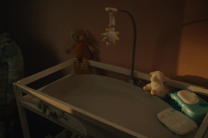 A closeup view of a baby changing table in a dimly lit room likely a nursery on the table various baby essentials are arranged including a baby mobile hanging above a teddy bear a soft toy lamb diapers and a pack of baby wipes