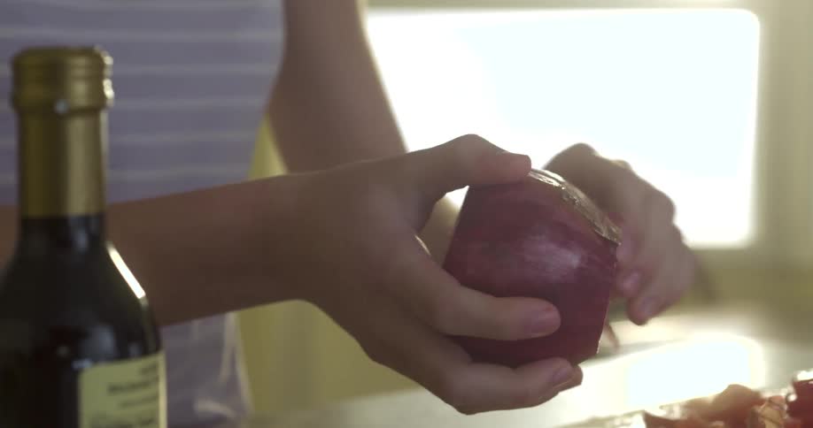 A woman peels skin off a red onion