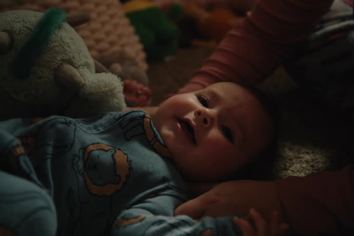 Hands of an adult tickling a baby lying on the carpet