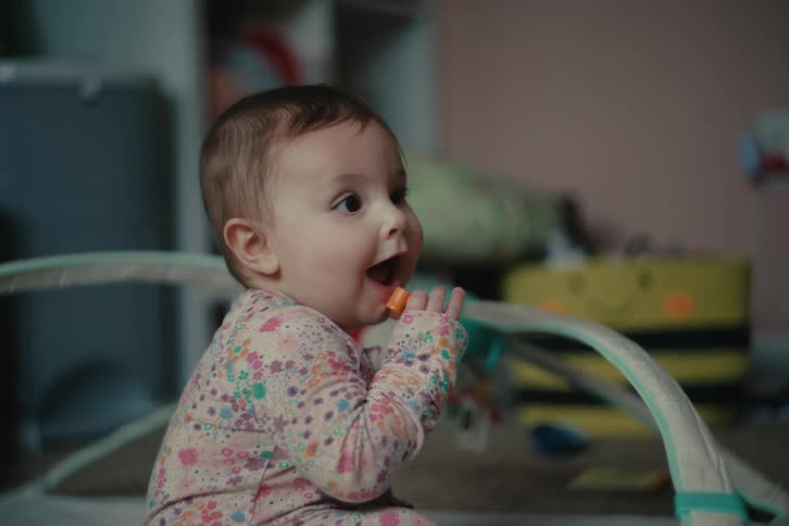 A baby sits on the floor playing with a toy and chewing on it