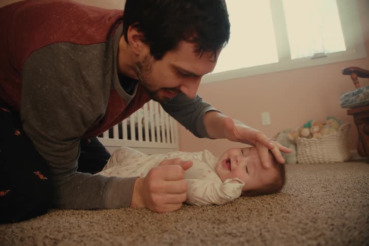 Father playing with his baby who is lying on the bedroom carpet