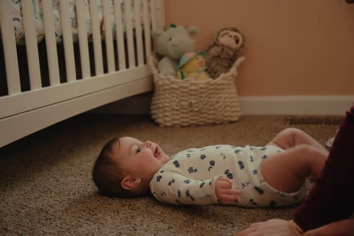 Adult person playing with a baby lying on the carpet