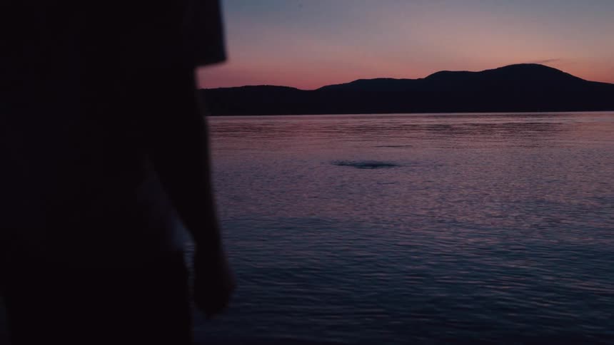Boy is skipping a rock on the lake at sunset