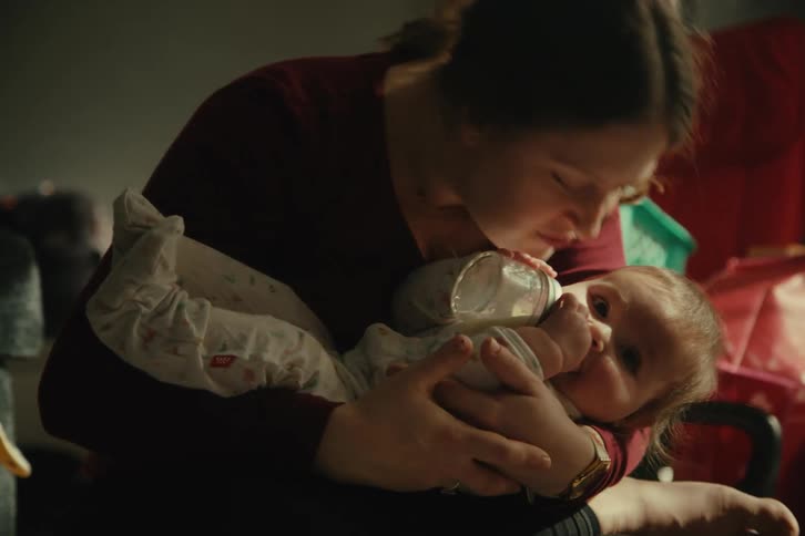 Mother kissing her baby in her arms while she is drinking milk from a bottle