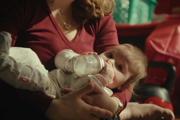 Baby drinking milk from a bottle while lying on her mothers lap