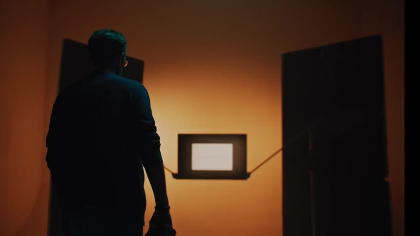 Silhouette of a person crouching with a professional camera in a lowlight studio