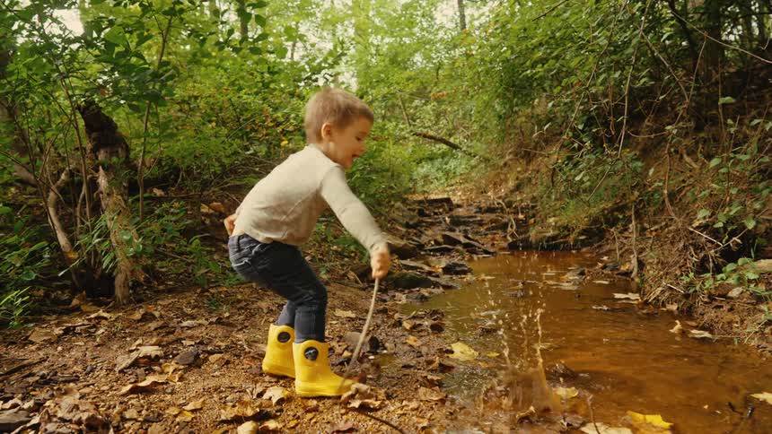 Boy throwing a stone into a river on a forest trail